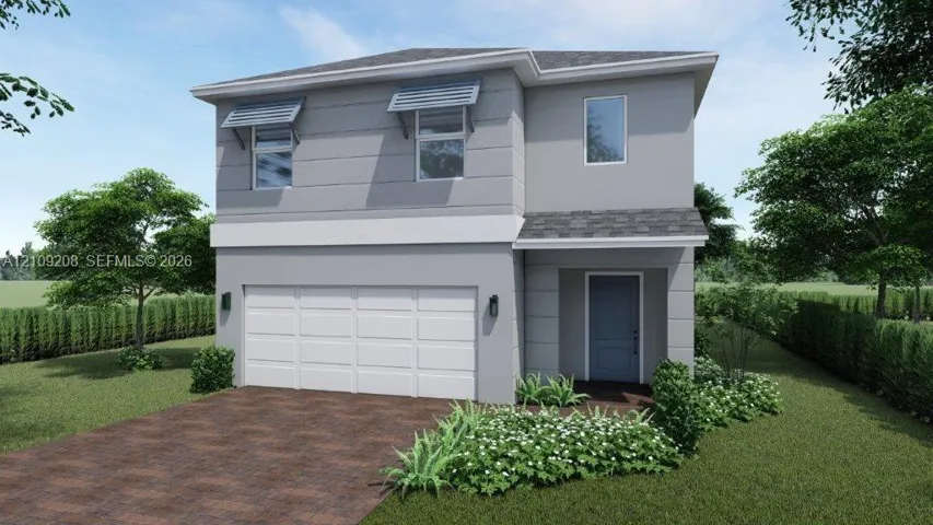 Two-story exterior featuring a stucco facade, double-car garage, paved driveway, upper-level metal awnings, and manicured landscaping