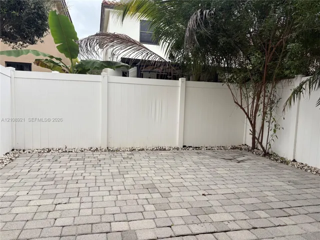 Paver patio featuring stone-finish block surfacing, bordered by decorative gravel and enclosed by a white vinyl privacy fence