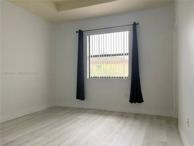 Interior room featuring tray ceiling, wood-finish flooring, and a single window with vertical blinds