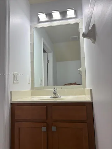 Wood-finish vanity cabinet, solid-surface countertop with integrated sink, chrome single-handle faucet, wall-mounted three-light fixture, and tile-framed mirror