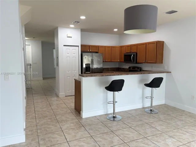 Kitchen featuring wood cabinetry, stainless steel refrigerator, built-in microwave, stone-finish breakfast bar, and tile flooring