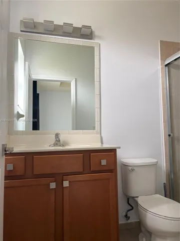 Bathroom vanity featuring warm-toned wood cabinetry, an integrated countertop with a single-basin sink, a framed mirror with tiled surround, and a four-light fixture