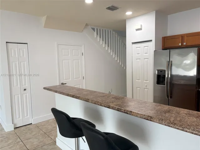 Kitchen featuring a breakfast bar with stone-finish countertop, stainless steel refrigerator, recessed lighting, and tile flooring