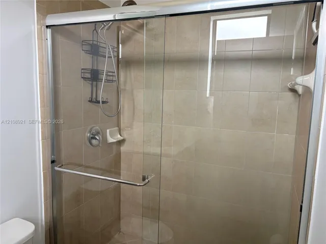 Walk-in shower enclosure featuring floor-to-ceiling neutral ceramic tiling, a sliding glass door with chrome hardware, and an integrated handheld shower fixture
