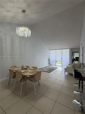 Vaulted ceilings, large-format tile flooring, decorative beaded chandelier, and floor-to-ceiling glass sliding doors with integrated shades