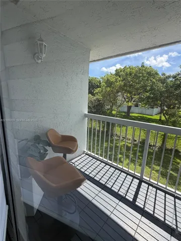 Private balcony featuring white vertical railing, textured stucco walls, overhead carriage-style lighting, and tiled flooring