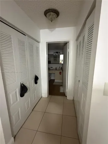 Hallway featuring large-format tile flooring and dual sets of white louvered-panel bi-fold closet doors, illuminated by a ceiling-mounted flush-mount light fixture