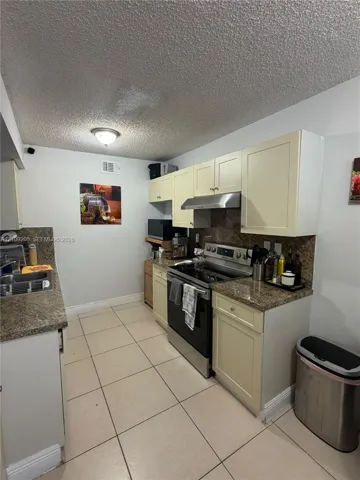 Kitchen featuring cream-toned shaker cabinetry, stone-finish countertops, stainless steel range with overhead hood, and tile flooring