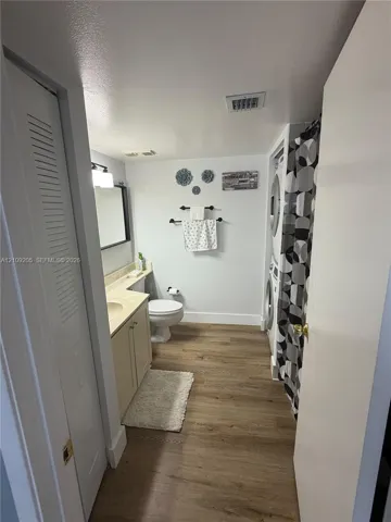Bathroom featuring wood-finish flooring, a vanity with a solid-surface countertop, and an integrated stacked laundry unit
