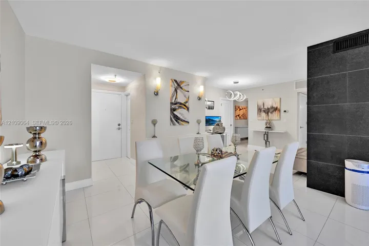 Open-concept interior featuring large-format tile flooring, a prominent black stone feature wall, dual wall-mounted light fixtures, and recessed ceiling lighting