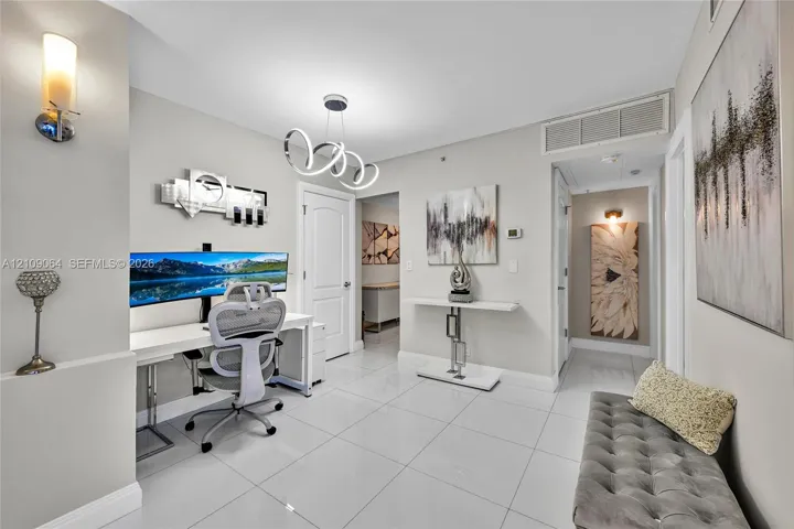 Open-concept space featuring polished tile flooring, a modern multi-ring sculptural chandelier, wall-mounted ambient sconce lighting, and a built-in recessed storage niche