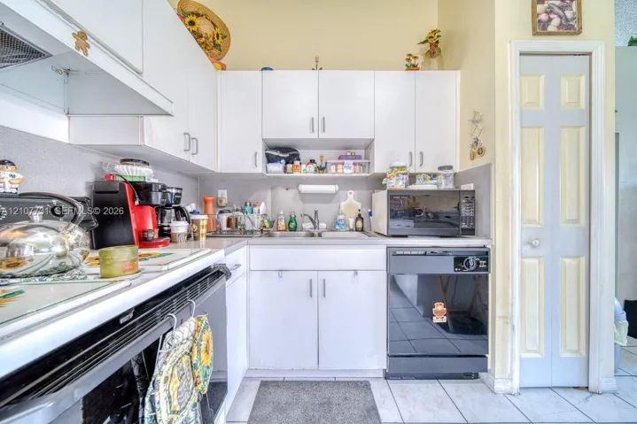 Kitchen featuring white cabinetry, solid-surface countertops, dual-basin stainless steel sink, black built-in dishwasher, and tile flooring