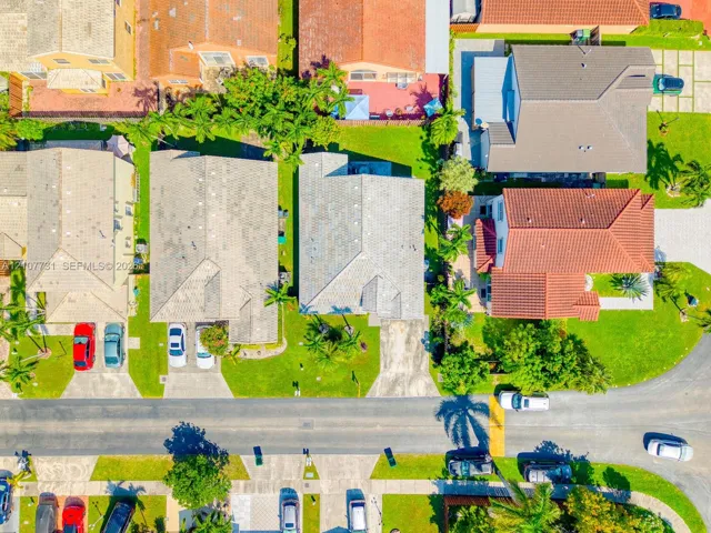 Aerial perspective featuring a residential lot with a paved driveway, front lawn, and mature landscaping