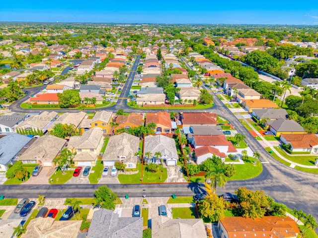 Aerial perspective of residential property featuring a concrete tile roof, attached garage, paved driveway, and established landscaping