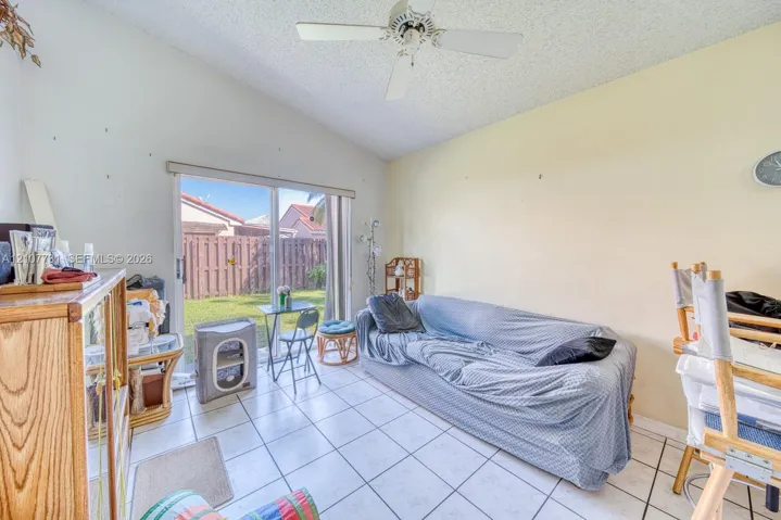 Vaulted ceiling with a white overhead fan, light-colored tile flooring, and a sliding glass door providing external access