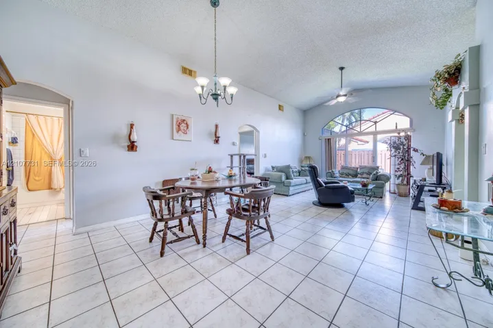 Open-concept living space featuring vaulted ceilings, arched entryways, tile flooring, an arched window, and an integrated hanging light fixture