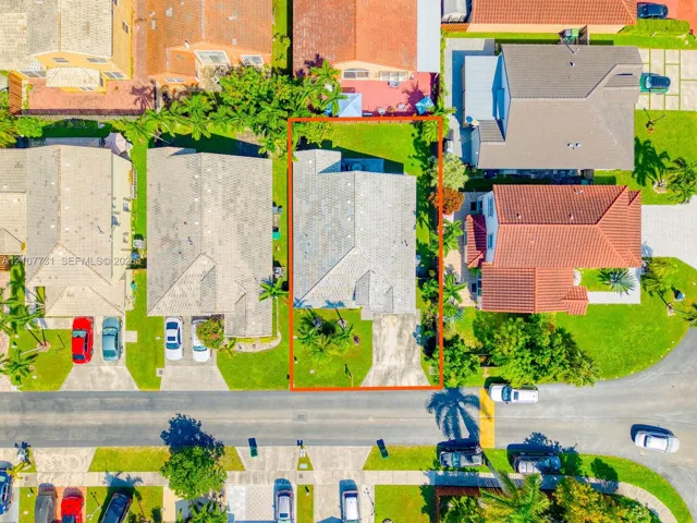 Aerial view of residential property featuring a concrete driveway, multi-gabled roofline, and fenced rear lawn