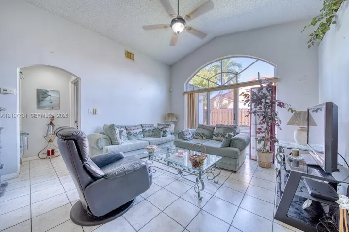 Vaulted ceilings, arched window, sliding glass door, and neutral ceramic tile flooring