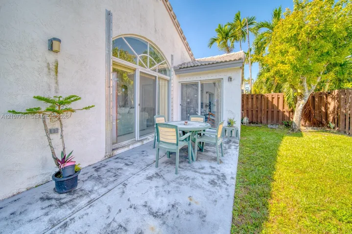Stucco exterior featuring an arched glass slider, concrete patio, grass lawn, and wood privacy fencing