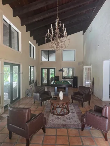 High vaulted ceilings with exposed dark wood beams, terracotta tile flooring, multi-light chandelier, and expansive windows