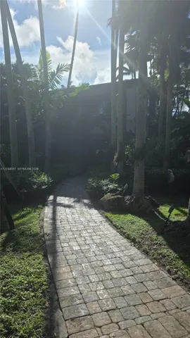 Paver stone walkway bordered by mature palm trees and established landscaping
