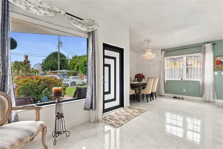 Large-format picture window, polished stone-finish flooring, custom geometric-patterned entry door, and tiered crystal chandelier