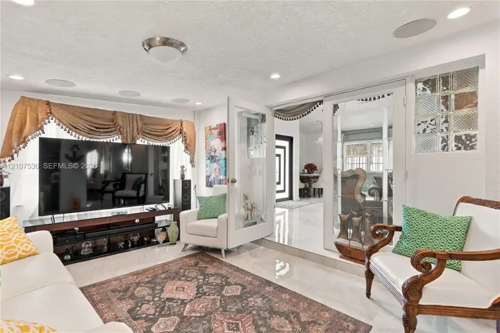 Living space featuring neutral stone-finish flooring, recessed lighting, integrated ceiling speakers, glass French doors, and decorative glass block accents