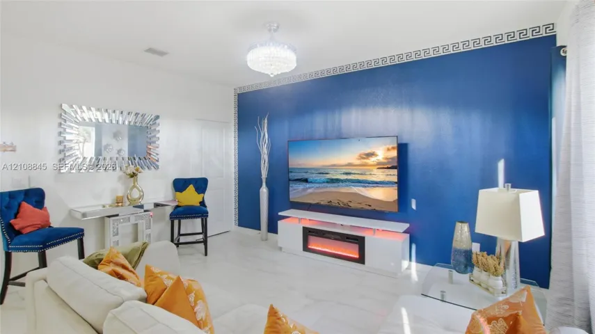 Accent wall featuring bold blue paint and intricate Greek key crown molding, complemented by white tile flooring and a crystal-style chandelier