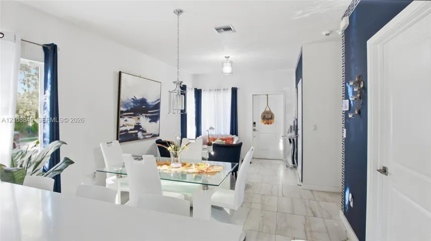 Open-concept interior featuring light-toned tile flooring, recessed ceiling lighting, a contemporary pendant light fixture, and a decorative accent wall