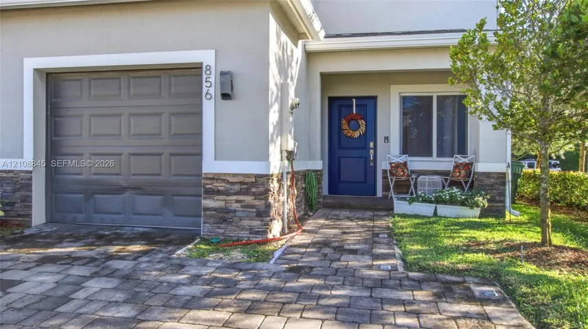 Stucco exterior facade featuring stone veneer masonry, paver walkway, single-car garage, and blue entry door