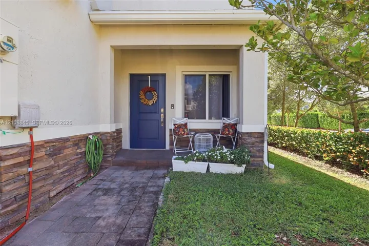 Covered entryway featuring a solid-color panel door, natural stone veneer siding, and a paver walkway