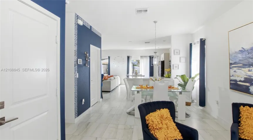Open-concept interior featuring large-format tile flooring, bold navy blue accent walls, decorative geometric trim, and a hanging pendant light fixture