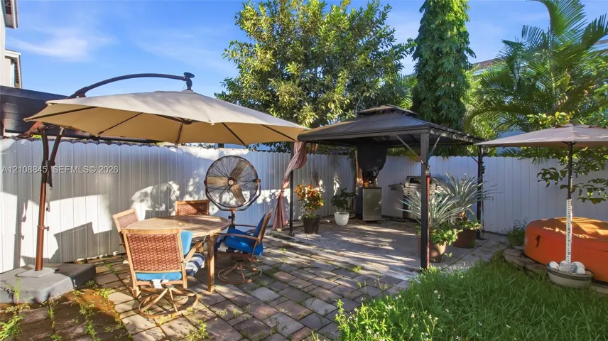 Enclosed rear patio featuring paver stone flooring, a metal-framed gazebo, and perimeter vinyl fencing