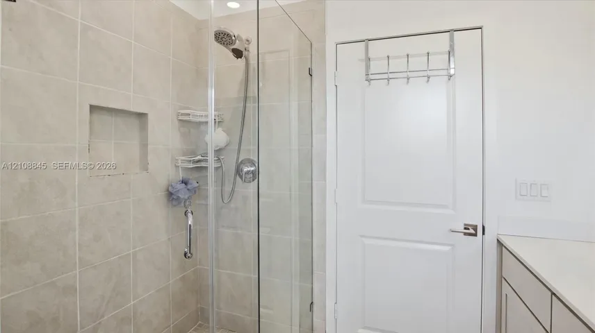 Walk-in shower featuring a frameless glass door, light-toned wall tile, a recessed niche, and a handheld showerhead fixture
