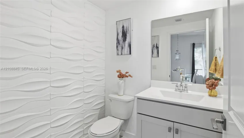 Bathroom featuring a textured three-dimensional wall treatment, vanity with a rectangular sink, countertop, and a large wall-mounted mirror