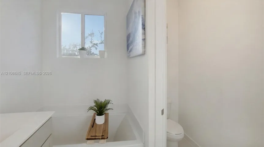Full-width soaking tub, clean-lined white cabinetry, quartz countertop, and integrated plumbing fixtures