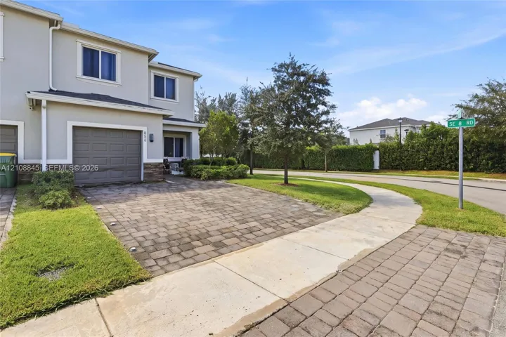Two-story exterior featuring a stone-veneer accent wall, paver driveway, single-car garage, and manicured landscaping