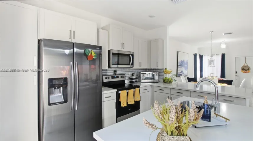 Kitchen featuring white shaker-style cabinetry, stainless steel appliances, a central island with a solid-surface countertop, and a tiled backsplash