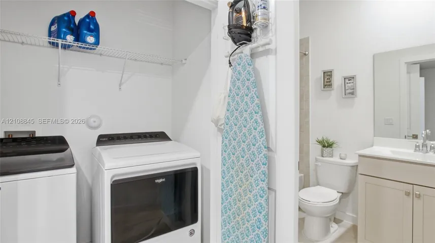 Laundry area featuring wire shelving, paired with a bathroom containing a vanity, rectangular sink, and toilet