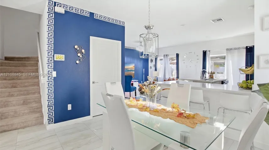 Open-concept interior featuring porcelain tile flooring, a custom-painted accent wall with decorative molding, a kitchen island with stone countertops, and a modern tiered chandelier
