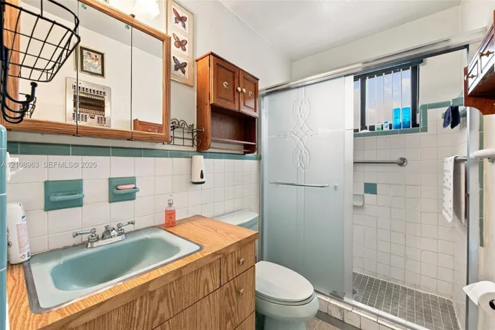 Bathroom featuring a wood vanity with a dual-handle faucet, integrated medicine cabinet, shower enclosure with glass sliding doors, and tiled wall accents