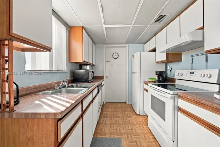 Kitchen featuring wood-trim cabinetry, laminate countertops, a dual-basin stainless steel sink, tile flooring, and integrated white appliances