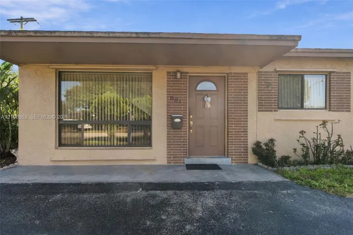 Single-story exterior featuring a stucco and brick facade, a covered entryway, and large horizontal windows
