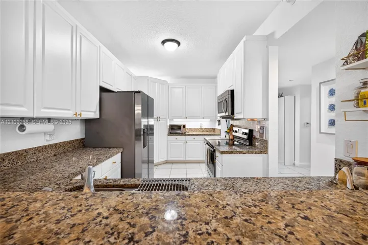 Kitchen featuring white cabinetry, stone-surface countertops, tile flooring, and stainless steel appliances