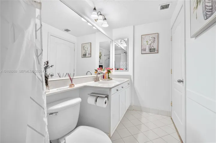 Bathroom featuring a white vanity cabinet with an integrated sink and countertop, full-width vanity mirror, polished metal fixtures, and diagonal tile flooring