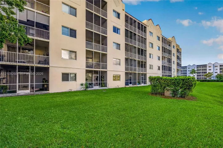 Multi-story stucco exterior featuring screened balconies, horizontal sliding windows, and manicured lawn space