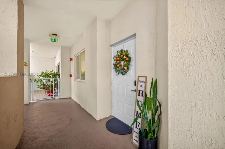 Covered exterior entryway featuring textured wall finishes, a solid core white paneled door, and metal railing enclosure