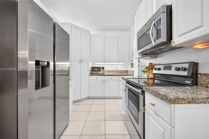 Kitchen featuring white cabinetry, stone-finish countertops, stainless steel appliances, and tile flooring