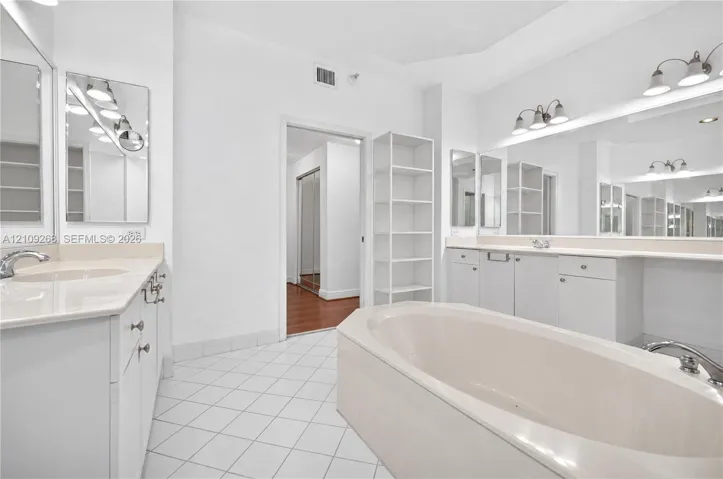 Dual-sink vanity with light-toned solid surface countertops, built-in shelving, large wall-mounted mirrors, and an expansive soaking tub