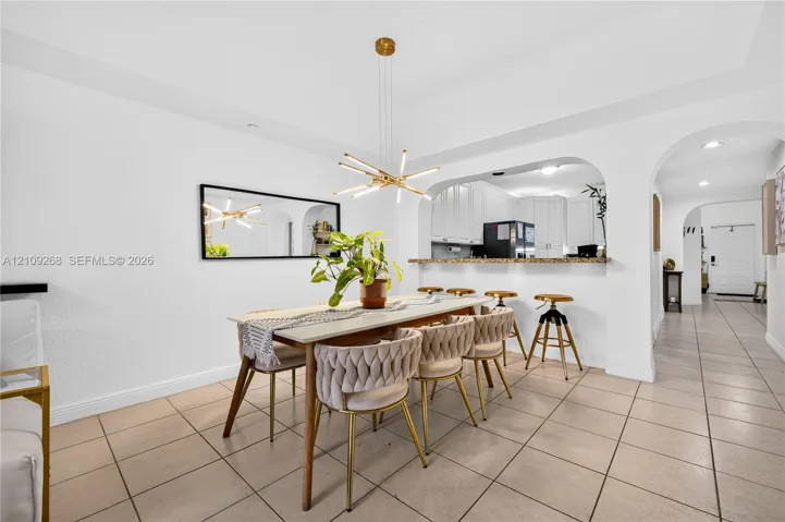 Dining area featuring tile flooring, a multi-light contemporary chandelier, arched architectural detailing, and a breakfast bar with stone-surface countertop